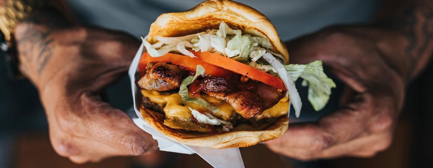 man holds a thick, juicy burger with both hands